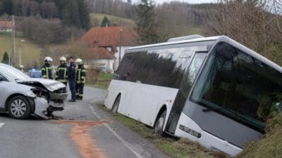 Beschädigtes silbernes Auto und weiß-grauer Linienbus im Straßengraben nach Unfall auf Landstraße