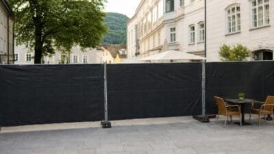 Schwarzer blickdichter Bauzaun auf einem gepflasterten Platz vor historischen Gebäuden