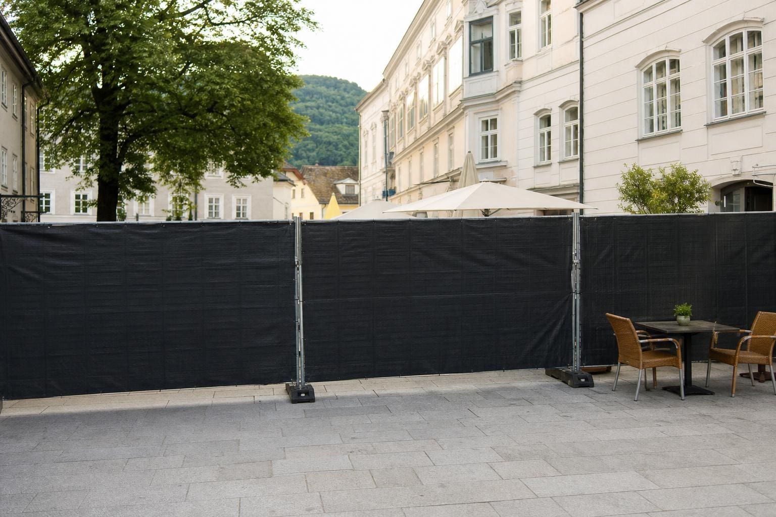 Schwarzer blickdichter Bauzaun auf einem gepflasterten Platz vor historischen Gebäuden