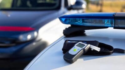 Ein digitales Alkoholmessgerät liegt auf der Motorhaube eines Polizeifahrzeugs mit Blaulichtbalken.