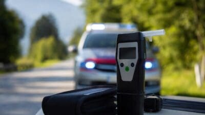 Nahaufnahme eines Alkoholtesters auf dem Armaturenbrett eines Autos mit einem Polizeiwagen und Blaulicht im Hintergrund