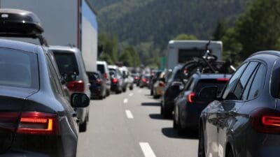 Mehrere Autos und ein LKW stehen im Stau auf einer Autobahn mit Bergen im Hintergrund