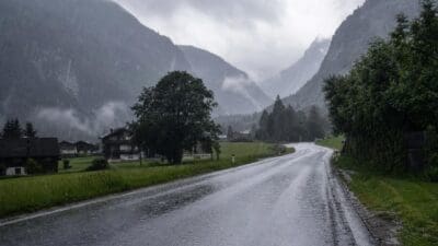 Nasse Landstraße schlängelt sich durch ein regnerisches Bergtal mit Häusern und Bäumen