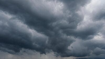 Dunkle Gewitterwolken mit Regen über einer hügeligen Landschaft