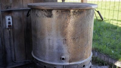 Rostiger zylindrischer Metallbehälter eines Futterdämpfers vor Holzwand mit Steuerungseinheit im Freien