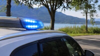 Blaulicht eines Polizeifahrzeugs leuchtet vor einem See und bewaldeten Bergen