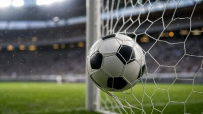 Ein schwarz-weißer Fußball steckt im Tornetz eines beleuchteten Stadions bei Regen