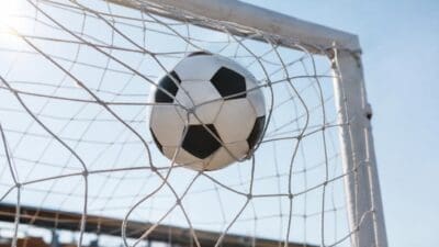 Schwarz-weißer Fußball steckt im weißen Netz eines Tores bei hellem Sonnenlicht