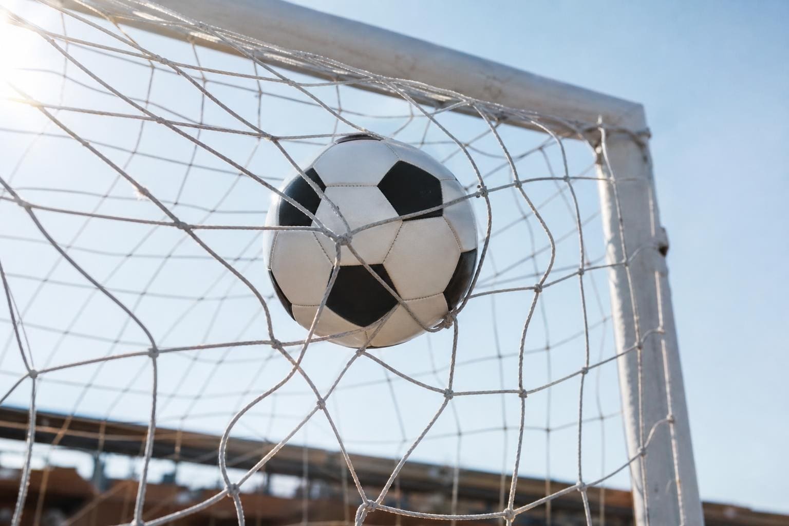 Schwarz-weißer Fußball steckt im weißen Netz eines Tores bei hellem Sonnenlicht