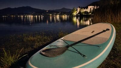 Türkises SUP-Board mit Paddel liegt am Ufer des Fuschlsees bei Nacht