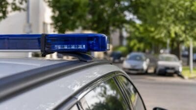 Blaues Blaulicht leuchtet auf dem Dach eines silbernen Polizeifahrzeugs auf einer Straße.