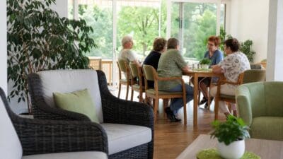 Ältere Frauen sitzen an einem Tisch in einem hellen Gemeinschaftsraum mit großen Fenstern.