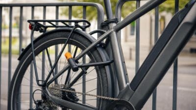 Nahaufnahme eines grauen E-Bikes mit einem Schloss am Hinterrad an einem Metallgeländer.