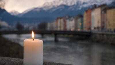 Eine brennende weiße Kerze steht auf einer Steinmauer vor verschwommenem Blick auf Innsbruck mit Inn und Nordkette.