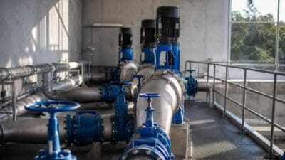 Blaue Pumpen und silberne Rohrleitungen in einer industriellen Wasseranlage mit Betonwänden und Fenstern