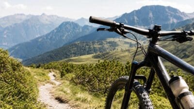 Lenker und Vorderrad eines Mountainbikes auf einem schmalen Pfad vor Bergpanorama