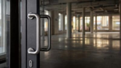 Silberner Türgriff an dunkler Tür mit Blick in leeren Hallenraum