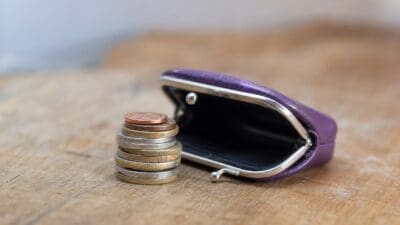 Offenes lila Portemonnaie neben einem Stapel Münzen auf einem Holztisch