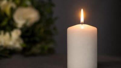 Eine brennende weiße Kerze mit unscharfen weißen Blumen im Hintergrund