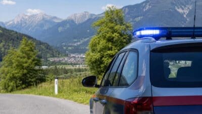 Polizeiauto mit blauem Blaulicht steht an einer Bergstraße vor Alpenkulisse