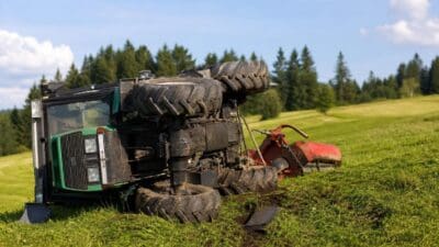 Umgekippter grüner Traktor mit großen Reifen und rotem Anbaugerät auf einer Wiese