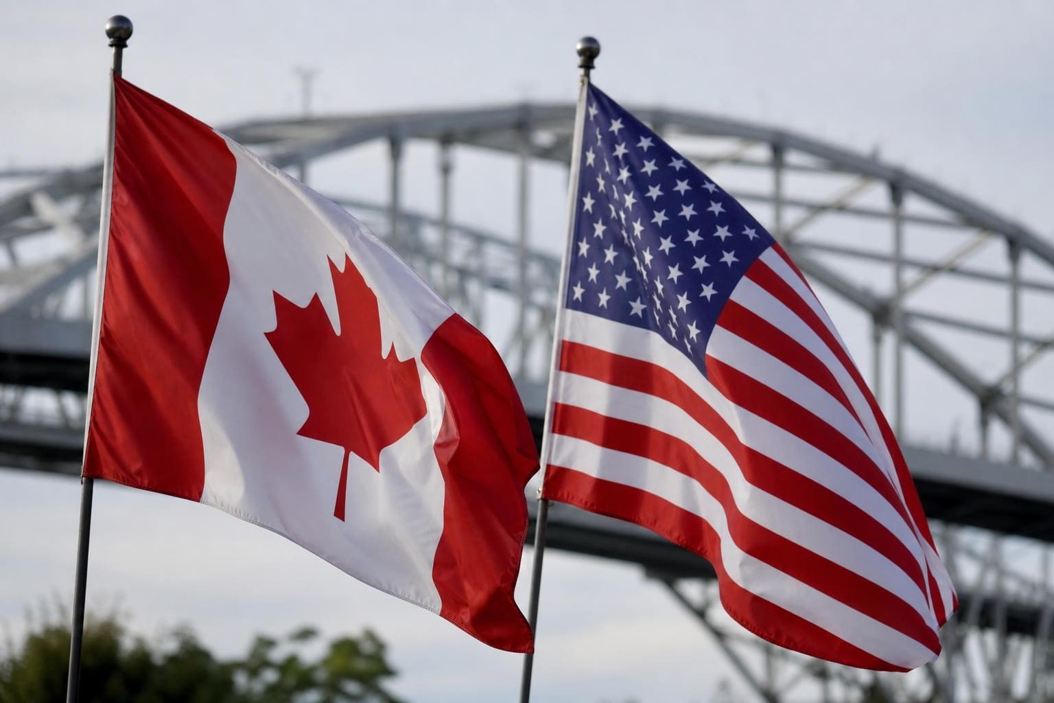 Kanadische und US-amerikanische Flagge wehen vor einer Stahlbrücke im Hintergrund