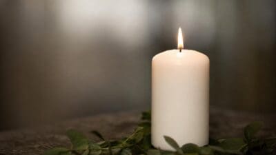 Brennende weiße Kerze mit grünen Zweigen auf dunkler Oberfläche
