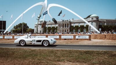 Silberner historischer Mercedes-Rennsportwagen fährt auf der Strecke vor Goodwood House
