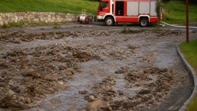 Rotes Feuerwehrauto steht neben einer schlammbedeckten Straße mit Steinen und Wasser