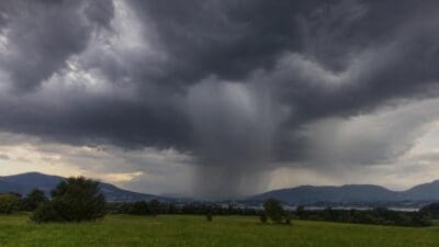 Dunkle Gewitterwolken mit Starkregen über grüner Wiese und Berglandschaft