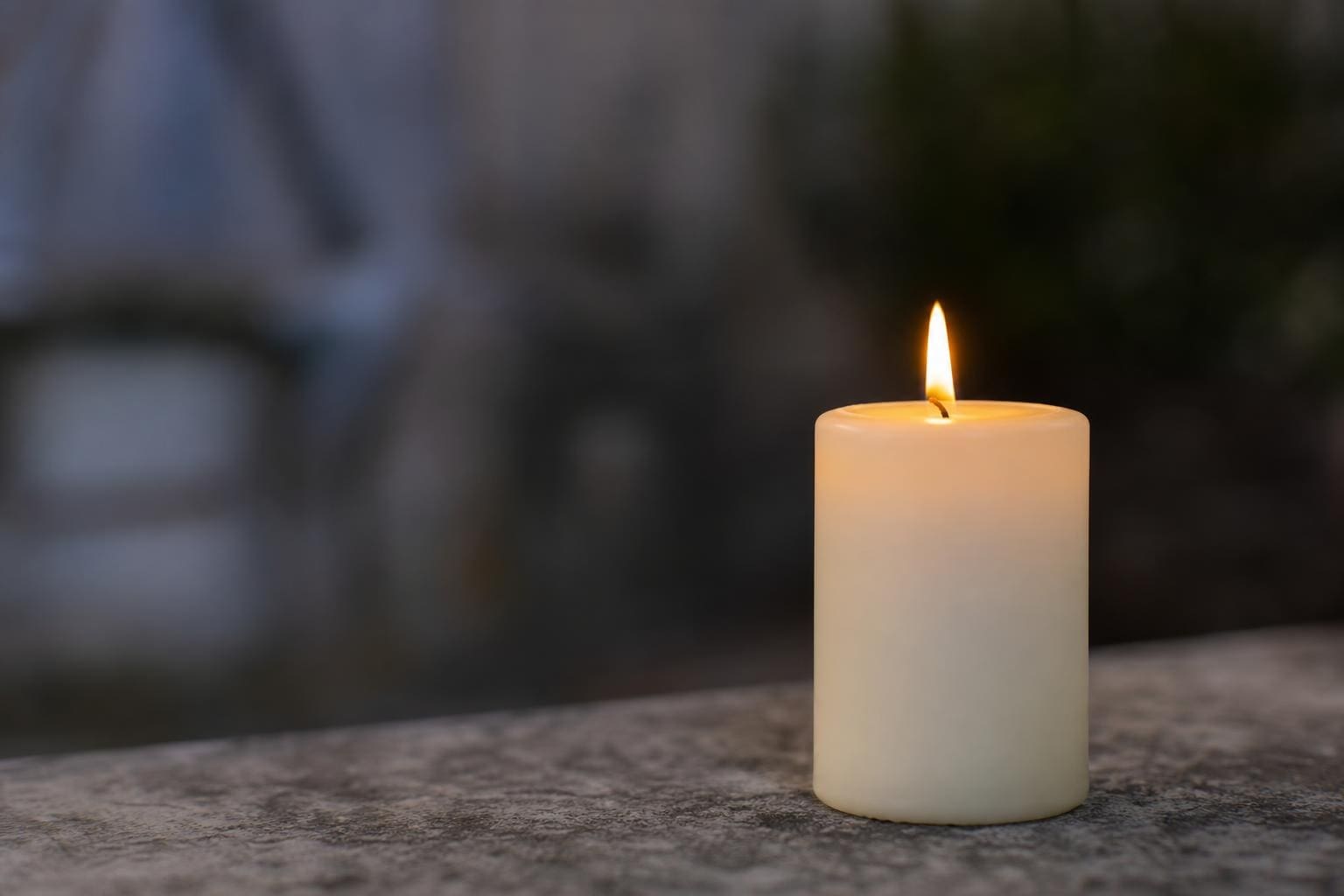 Weiße brennende Stumpenkerze mit gelber Flamme auf steinerner Fläche