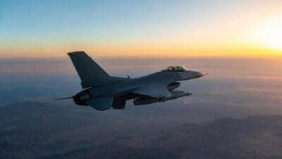 Graues Kampfflugzeug fliegt über bergige Landschaft bei Sonnenaufgang oder Sonnenuntergang