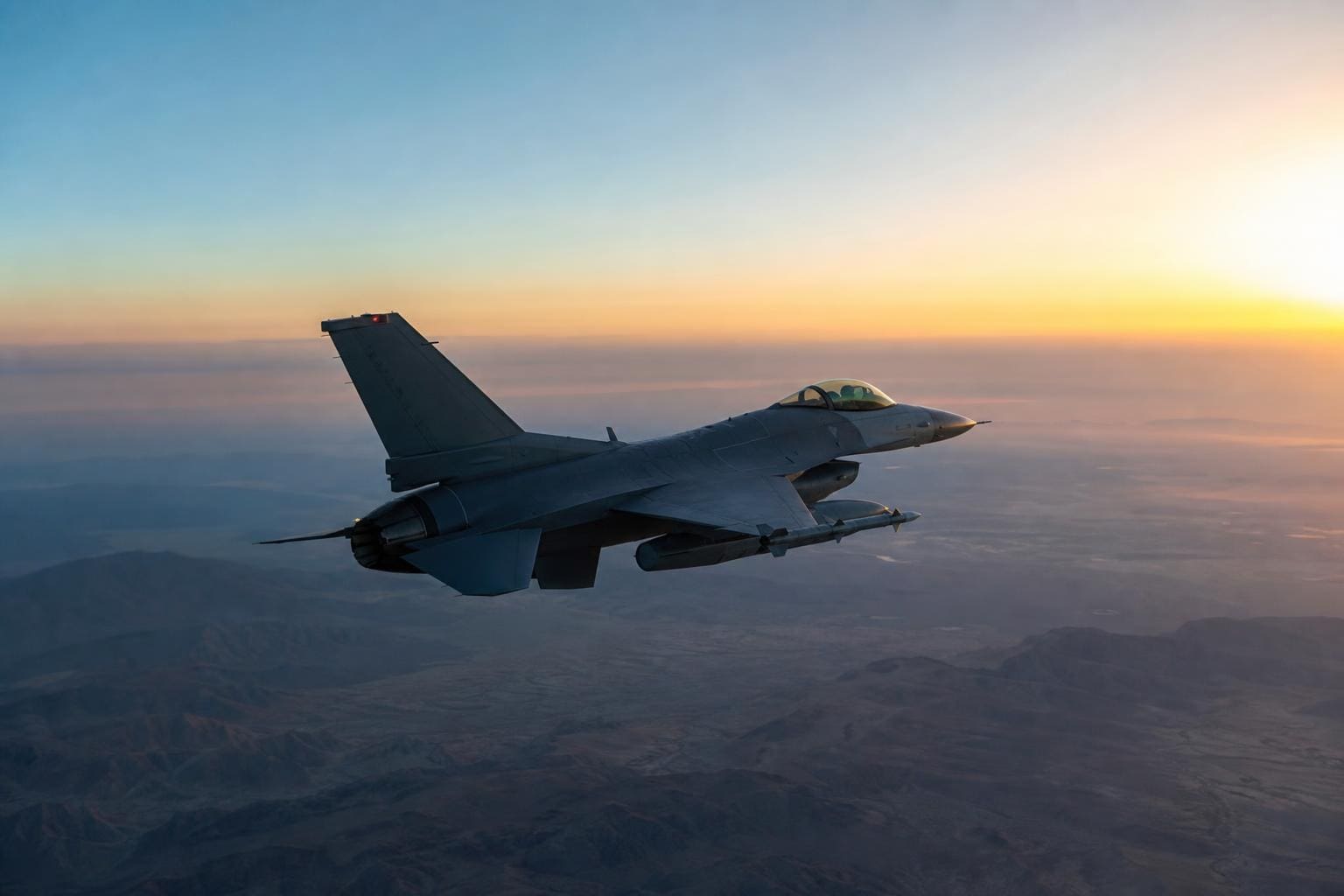 Graues Kampfflugzeug fliegt über bergige Landschaft bei Sonnenaufgang oder Sonnenuntergang