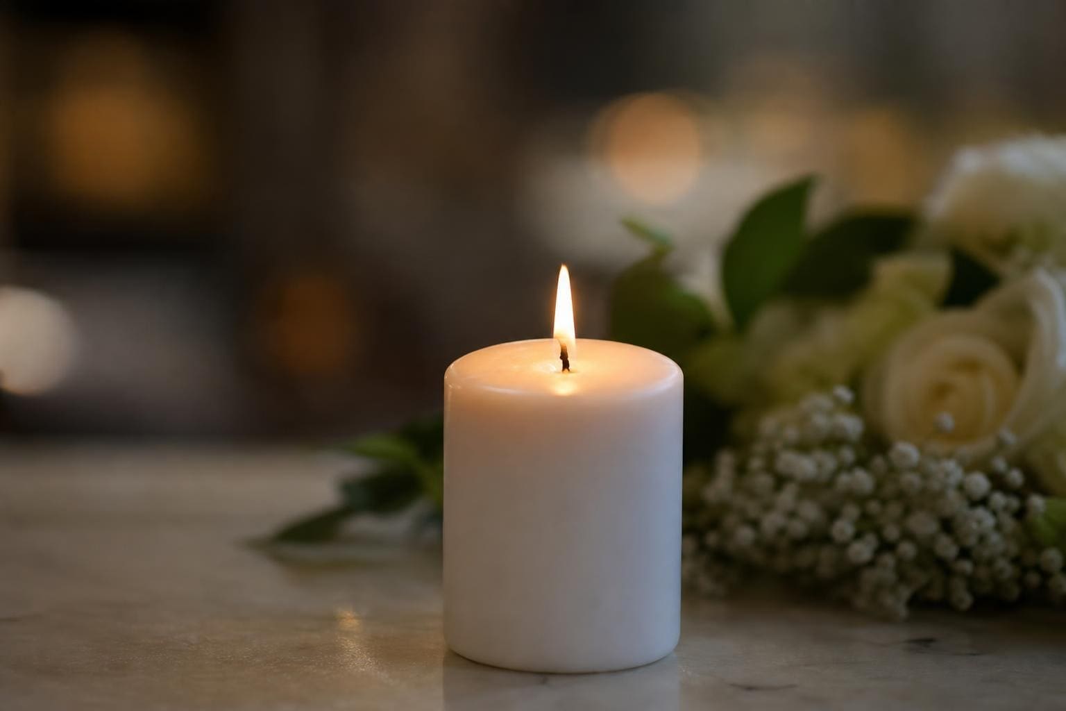Eine brennende weiße Kerze auf einer Marmorplatte neben weißen Rosen und Schleierkraut