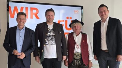 Vier Männer und ein schwarzer Hund stehen vor einem Bildschirm mit SPÖ-Logo.