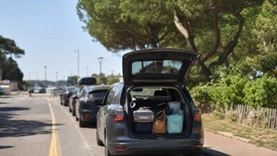 Graues Auto mit offenem Kofferraum voller Koffer und Taschen auf einer Straße.