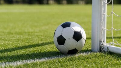 Schwarz-weißer Fußball liegt auf grünem Kunstrasen neben einem Torpfosten