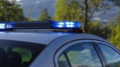 Leuchtende blaue Blaulichtleiste auf dem Dach eines silbernen Einsatzfahrzeugs vor Bäumen und Bergen