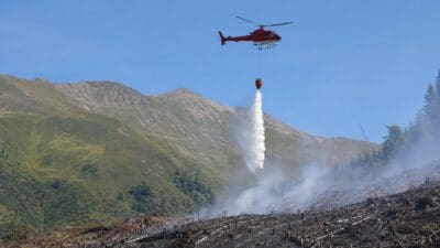 Roter Hubschrauber löscht mit Wasser aus einem Behälter einen Waldbrand in den Bergen