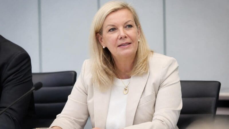 Blonde Frau in hellem Blazer sitzt an einem Tisch in einem Konferenzraum und blickt zur Seite