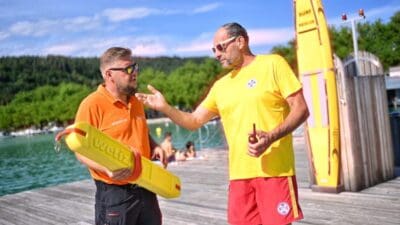 Zwei Rettungskräfte stehen auf einem Holzsteg am See und besprechen sich mit Rettungsboje.
