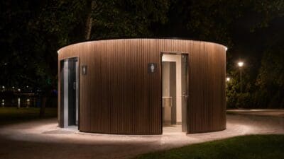 Rundes hölzernes WC-Gebäude mit offenen Türen und beleuchteten Symbolen in der Nacht