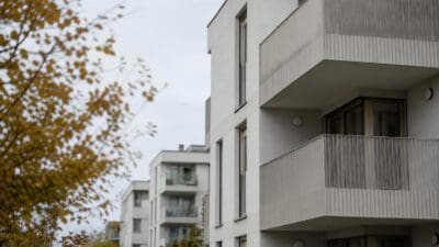 Moderne weiße Wohngebäude mit Balkonen und vertikalen Lamellen sowie Bäumen im Vordergrund