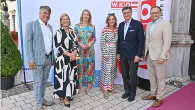 Sechs Personen in eleganter Kleidung stehen vor Werbebannern der WKO Kärnten und lächeln in die Kamera.