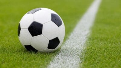 Ein schwarz-weißer Fußball liegt auf grünem Rasen neben einer weißen Linie.