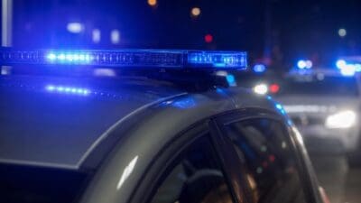 Blaues Blaulicht auf dem Dach eines Polizeifahrzeugs bei Nacht mit weiteren Einsatzfahrzeugen im Hintergrund