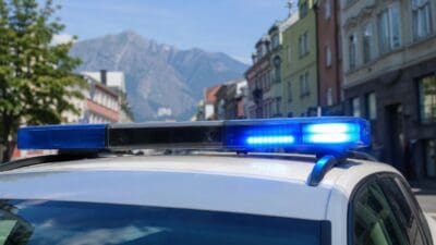 Blaues Blaulicht auf dem Dach eines weißen Polizeiautos mit Bergen im Hintergrund