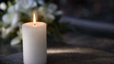Brennende weiße Kerze auf dunkler Oberfläche vor unscharfen weißen Blumen