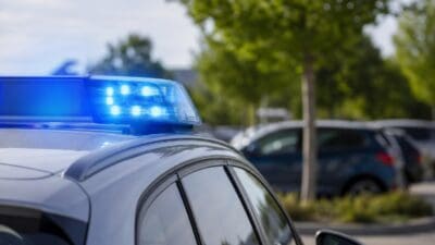 Polizeifahrzeug mit aktiviertem Blaulicht auf einem Parkplatz zwischen Bäumen und Autos