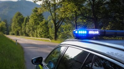 Polizeifahrzeug mit aktiviertem Blaulicht auf einer kurvigen Straße in einer grünen Berglandschaft